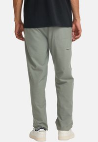 Light green, soft fabric pants with a slim fit, featuring a back pocket and finished with white sneakers.
