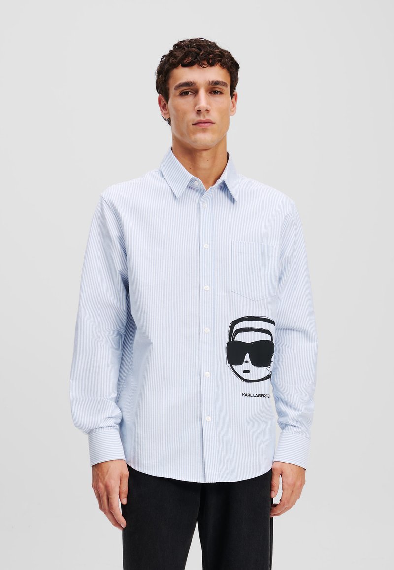 Light blue striped long-sleeve shirt featuring a chest pocket and a large black graphic of sunglasses and a face on the front.