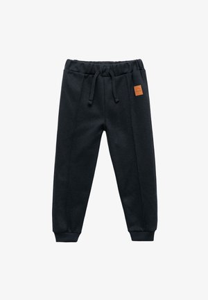 Czarne spodnie dresowe wykonane z miękkiego materiału, z elastycznym paskiem w talii ze sznurkiem, ściągaczami na końcach nogawek oraz małą brązową skórzaną naszywką z logo.