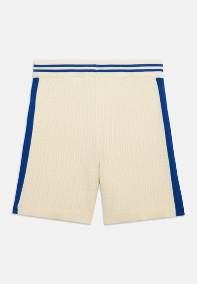 Shorts en maille crème avec bandes latérales bleues, ceinture côtelée avec deux bandes horizontales bleues et motif en maille torsadée texturée.