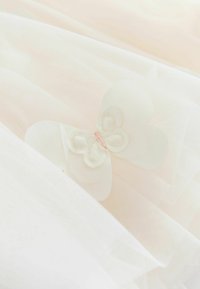 Zarter weißer transparenter Stoff mit geschichteter Textur, verziert mit einem kleinen weißen Stoffschmetterling mit pinken Stickereien.