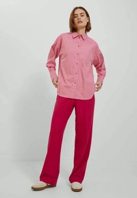 Stripete skjorte i rosa med lange ermer og krage; kombinert med løstsittende, lys rosa bukser. Nøytrale sko.