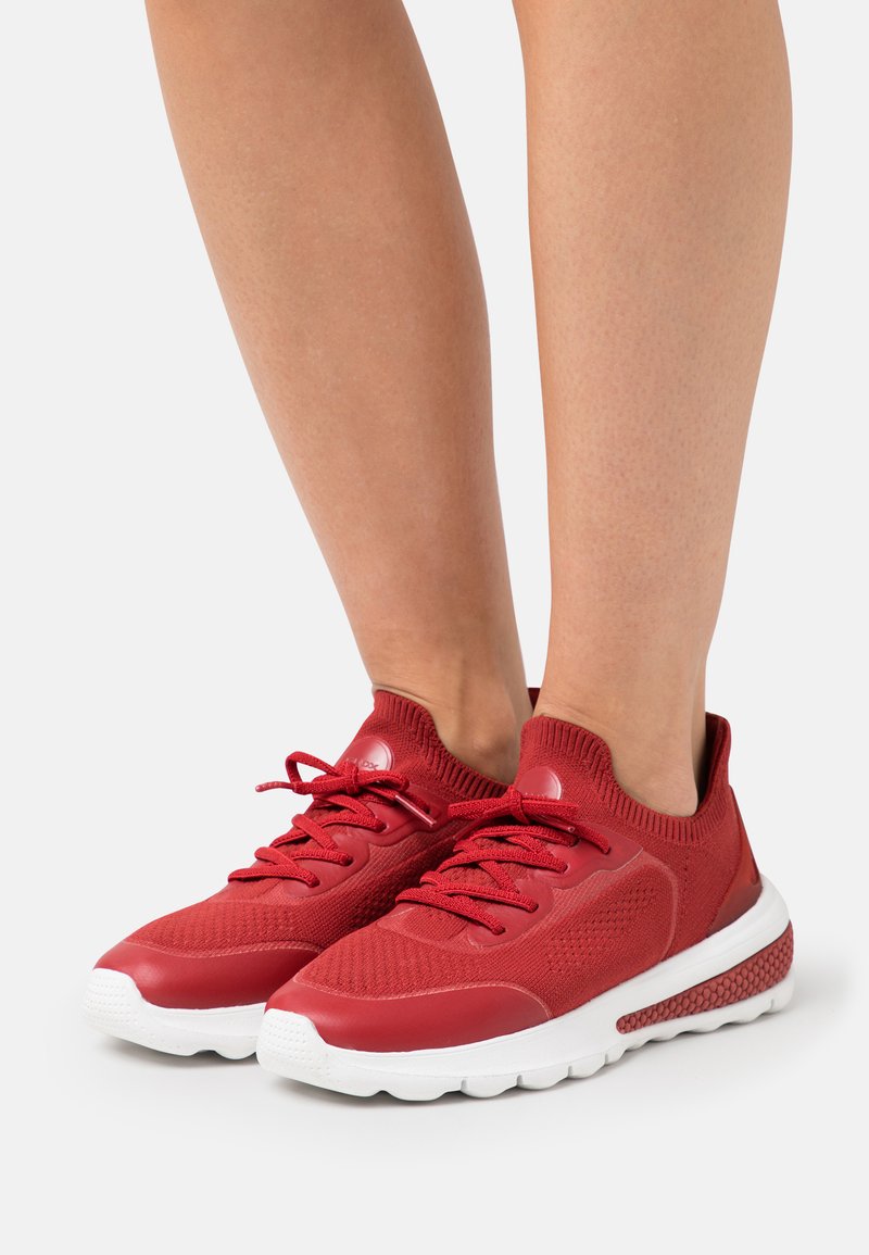 Scarpe sportive rosse con tomaia in rete, sovrapposizioni testurizzate e suola in gomma bianca. Presentano un collare imbottito alla caviglia e chiusura con lacci.