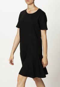 Robe noire avec un encolure arrondie, des manches courtes et une jupe évasée. Fabriquée à partir d'un tissu lisse, elle présente des éléments de design minimalistes.