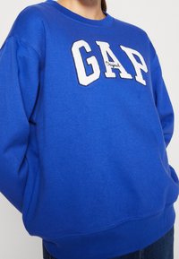 Sudadera azul con el logo "GAP" en bordado de fieltro blanco. Cuenta con un cuello redondo y un corte holgado, confeccionada en suave material de algodón.