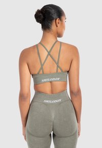 Conjunto de entrenamiento en verde oliva que incluye un sujetador deportivo con tirantes y diseño de espalda cruzada y leggings de cintura alta, ambos con detalles de logotipo.
