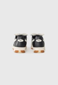 Zwarte sportieve schoenen met een glad leren bovenkant en een gestructureerde rubberen zool. Kenmerken zijn onder andere een wit PUMA-logo en contrasterende lichte accenten.