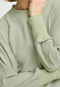 Maglione verde chiaro con un collo a coste alte, maniche voluminose e tessuto testurizzato con una vestibilità rilassata.