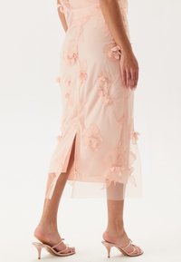 Ljust rosa spetsklänning med blommönster, knälängd, genomskinlig överdel, sidoflik, matchad med rosa klacksandaler.