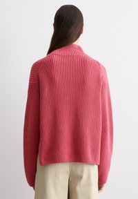 Strickpullover aus strukturiertem rosa Material mit weitem Kragen und überschnittenen Schultern, ausgestattet mit Rippendetails und einem verkürzten Saum, kombiniert mit beigen Hosen.