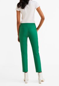 Pantalon vert sur mesure à coupe slim, doté de poches arrière et d'une texture lisse. Associé à des bottines blanches.