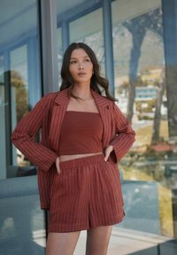 Tenue couleur rouille comprenant un blazer oversized à rayures, un top sans bretelles ajusté et un short coordonné avec une taille élastique.