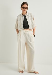 Camicetta bianca corta, canottiera nera aderente, pantaloni beige larghi con vita elastica e sandali bassi. Design minimalista con tasche.