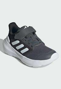 Black athletic shoe with mesh upper, gray accents, and Velcro strap. Features thick white sole and three white side stripes.
