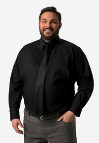Camicia nera a maniche lunghe con colletto e taschino frontale, abbinata a una cravatta nera e pantaloni grigi. Texture liscia, vestibilità classica.