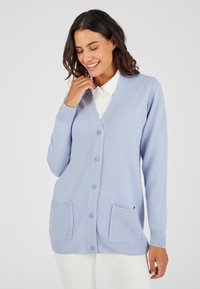 Cardigan lavorato a maglia blu chiaro con scollatura a V, cinque bottoni, polsini e orlo a costine e due tasche frontali. Realizzato in tessuto morbido.