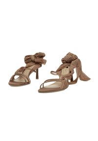 Sandalias de tacón marrones con un acento de lazo de tela translúcida en el tobillo, diseño de punta abierta y correas delgadas con un acabado texturizado.