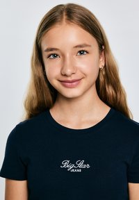 Tamsiai mėlyna marškinėliai su trumpomis rankovėmis, apvalia iškirpte ir baltu siuvinėtu "Big Star JEANS" logotipu priekyje. Sklandi medžiagos tekstūra.