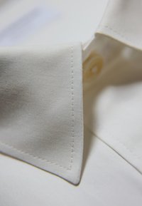 Close-up van een frisse witte shirtkraag met zichtbare stiksels en een beige knoop onder de gevouwen stof.
