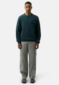 Sudadera en teal oscuro con un bolsillo, combinada con pantalones cargo gris claro. La sudadera tiene escote redondo y puños acanalados. Incluye calzado casual.