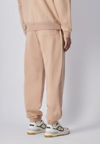Pantalones de chándal de algodón beige con puños elásticos y un bolsillo trasero, combinados con zapatillas blancas con acentos en gris y amarillo.