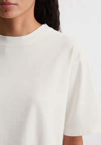 T-shirt in cotone crema con vestibilità rilassata, maniche corte e scollatura rotonda. Texture morbida e design semplice senza fantasie o accenti.