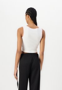 Hvit, kort tanktopp med rosa bølgekant, kombinert med svarte, løstsittende bukser som viser en glatt stoffoverflate og enkel design.