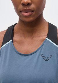 Κοντινό πλάνο ενός ατόμου που φοράει μπλε και μαύρο αθλητικό τοπ με μικρό μαύρο λογότυπο ζώου στο στήθος.