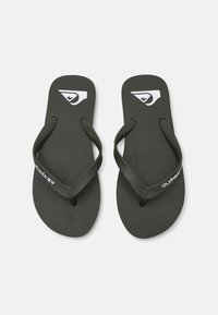 Fekete strandpapucs, textúrált talppal, vékony pántokkal és fehér logóval. A design minimalista stílust és könnyű anyagot jellemzi.