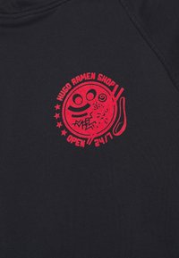 Tela negra con un gráfico circular rojo que presenta una cara sonriente estilizada, palillos, y el texto "HUGO RAMEN SHOP ABIERTO 24/7."