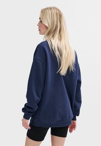 Marineblauwe sweater met een ontspannen pasvorm en verlaagde schouders. Lange mouwen en geribde boorden. Materiaal lijkt zacht met een gladde textuur.