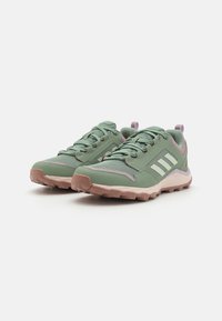 Groene sportieve schoenen met een gestructureerde mesh bovenkant, lichtroze accenten, drie witte strepen en een robuuste zool ontworpen voor grip.
