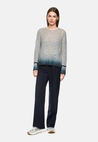 Leichter Strickpullover mit einem Farbverlauf von hellgrau zu tiefblau am Saum, kombiniert mit navyblauen weiten Hosen und Sneakers.
