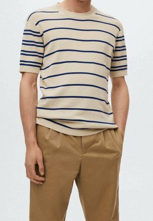 Suéter beige de manga corta con rayas horizontales azules, cuello redondo y ajuste relajado. Combinado con pantalones plisados de color marrón claro.