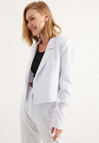 Vit rutig cropped blazer med skräddarsydd passform, med en enkel knappstängning och åtdragna ärmar. Bärs över en svart topp.