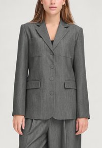 Blazer grigio su misura con due tasche frontali, chiusura con bottone a un solo petto e rever a scollo. Tessuto strutturato con un sottile motivo a righe.