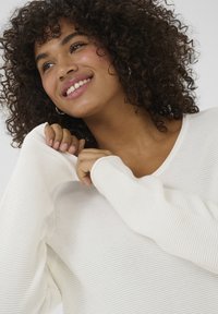 White ribbed sweater with a wide neckline and long sleeves. The fabric appears soft and textured, featuring subtle horizontal lines.