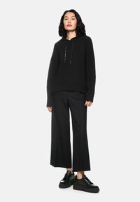 Schwarze gestrickte Kapuzenjacke mit gerippter Textur, ausgestattet mit einem Kordelzug, kombiniert mit weiten schwarzen Hosen und schwarzen Plateausneakern.