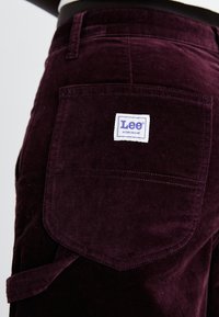 Bordeaux corduroy broek met een achterzak met een witte "Lee Workwear" label en een stoffen lus voor extra detail.