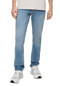 Jasnoniebieskie dżinsy o prostym kroju, z średnim praniem, subtelnym blaknięciem i klasycznym pięciokieszeniowym wzornictwem. Noszone z białymi trampkami.
