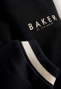 Tissu noir avec le texte « BAKER by Ted Baker » et un bord de manche rayé noir et blanc.