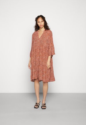 Vestido floral vermelho com decote em V, mangas bufantes três quartos, silhueta solta e design em camadas. Usado com sandálias pretas de tiras.