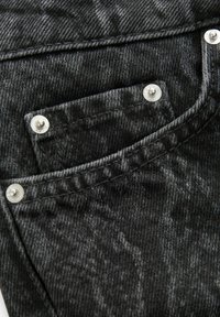 Tăietură din denim negru cu o suprafață texturată, având un buzunar gri și nasturi argintii. Cusăturile vizibile adaugă detaliu designului.