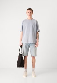 Lyseblå oversized T-shirt med korte ærmer, denimshorts, hvide sneakers og en sort tote-bag. Tekstiler med struktur, afslappet design.