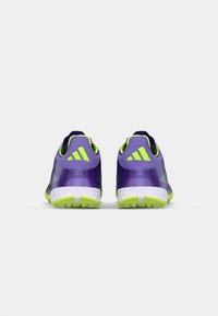 Scarpe da atletica viola con accenti verdi, caratterizzate da una tomaia testurizzata, un sistema di allacciatura e una suola bianca con tacchetti per la trazione.