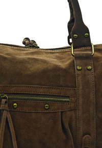 Sac à main en daim marron avec des éléments en laiton, comportant une poche zippée et une texture douce. Les accents incluent des coutures décoratives et des pompons.