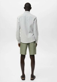 Maglietta a maniche lunghe a righe in grigio chiaro, abbinata a pantaloncini verde oliva. Il modello indossa sandali neri; attenzione ai materiali e ai colori.