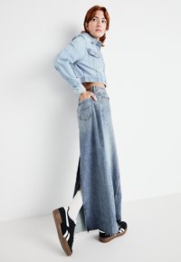 Giacca di jeans cropped azzurra, gonna in denim sbiadita a vita alta, sneakers nere con suola in gomma, calze bianche a tubo, fessure laterali sulla gonna.