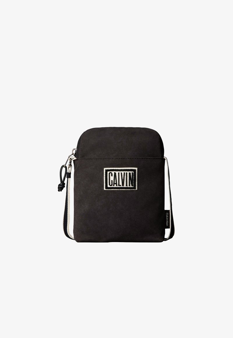 Μικρό μαύρο τσαντάκι crossbody με μπροστινή τσέπη, ασημένιο φερμουάρ και λευκή ετικέτα με την ένδειξη "CALVIN" με έντονα γράμματα.