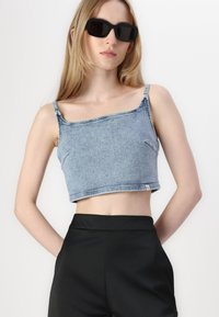 Plavi traper cropped top s tankim naramenicama i nerazrezanim rubom. Crne hlače visokog struka i tamne sunčane naočale upotpunjuju izgled.